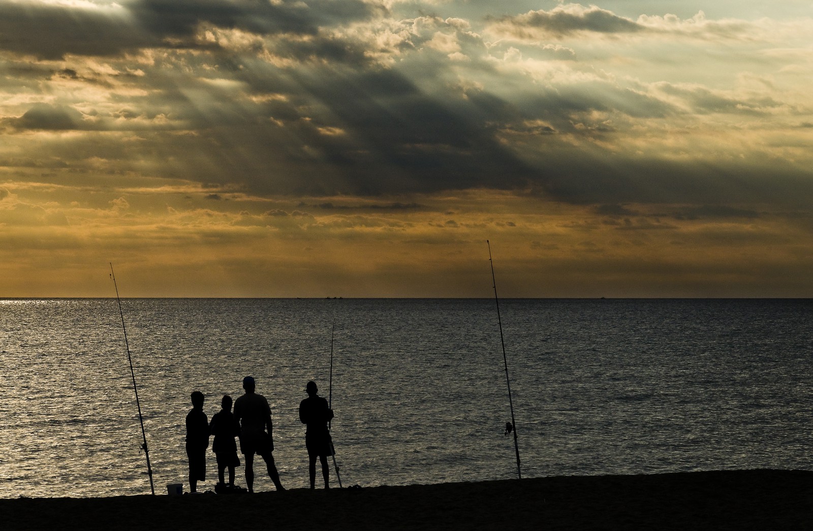 Silhouettes de pêcheurs à la ligne sur la plage au lever du soleil. - Silhouettes of anglers on the beach at sunrise.