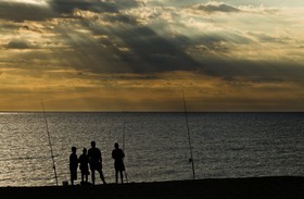 Silhouettes de pêcheurs à la ligne sur la plage au lever du soleil. - Silhouettes of anglers on the beach at sunrise.